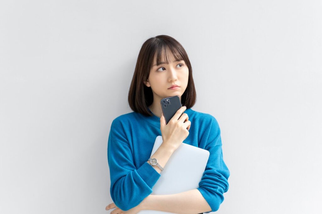 スマホとパソコンを持って考える女性（写真AC）